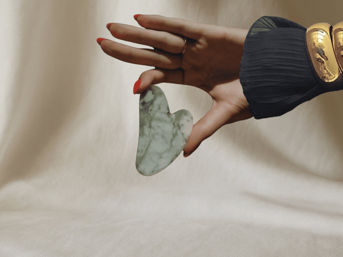 Hand holding a jade Gua Sha stone against skin, symbolizing ancient facial sculpting ritual rooted in Traditional Chinese Medicine.